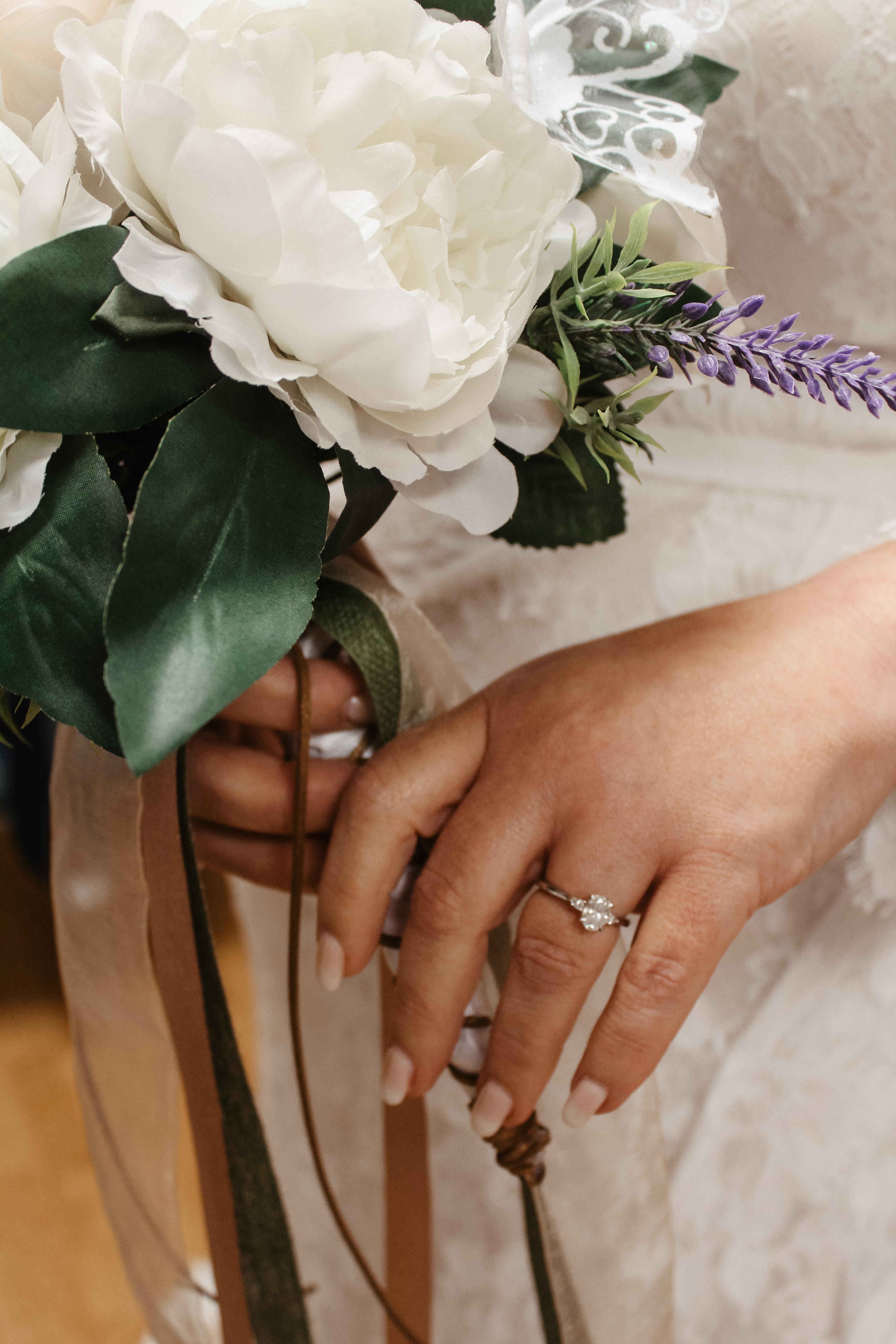 Bride holding floral bouquet, close-up of engagement ring and ribbon details