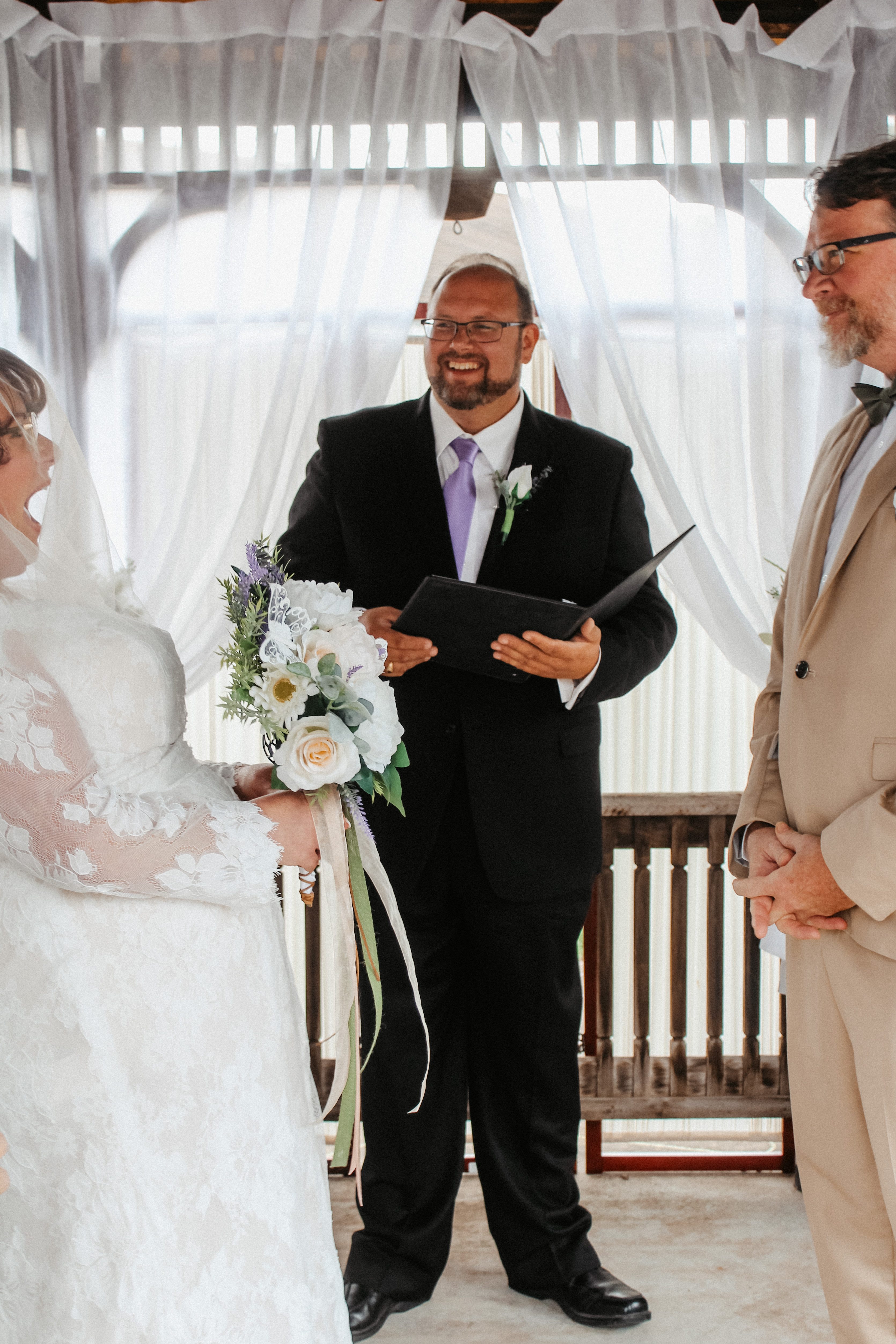 Officiant smiling at bride and groom, joyful wedding moment under gazebo