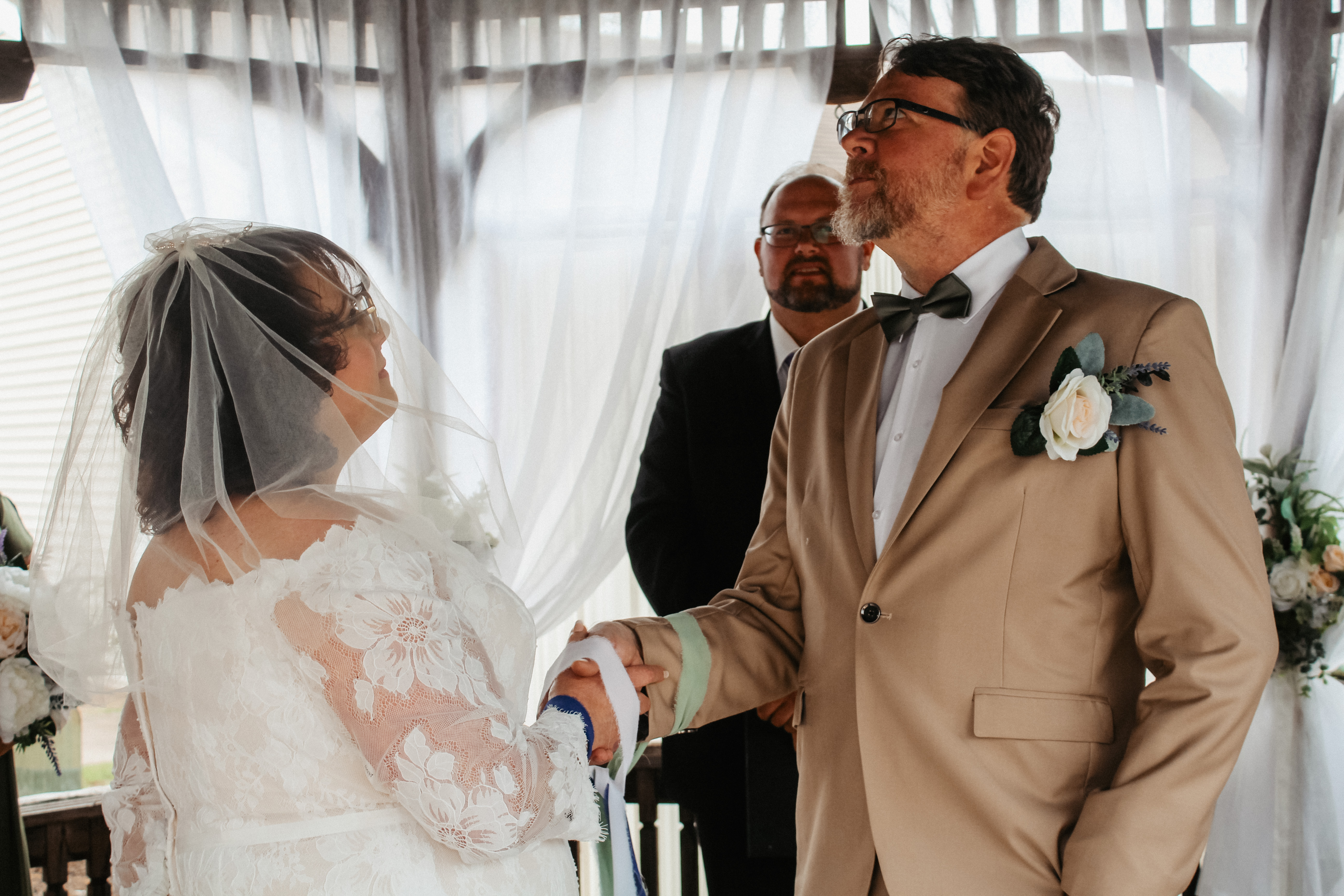 Bride and groom handfasting ceremony, exchanging vows under white drapery