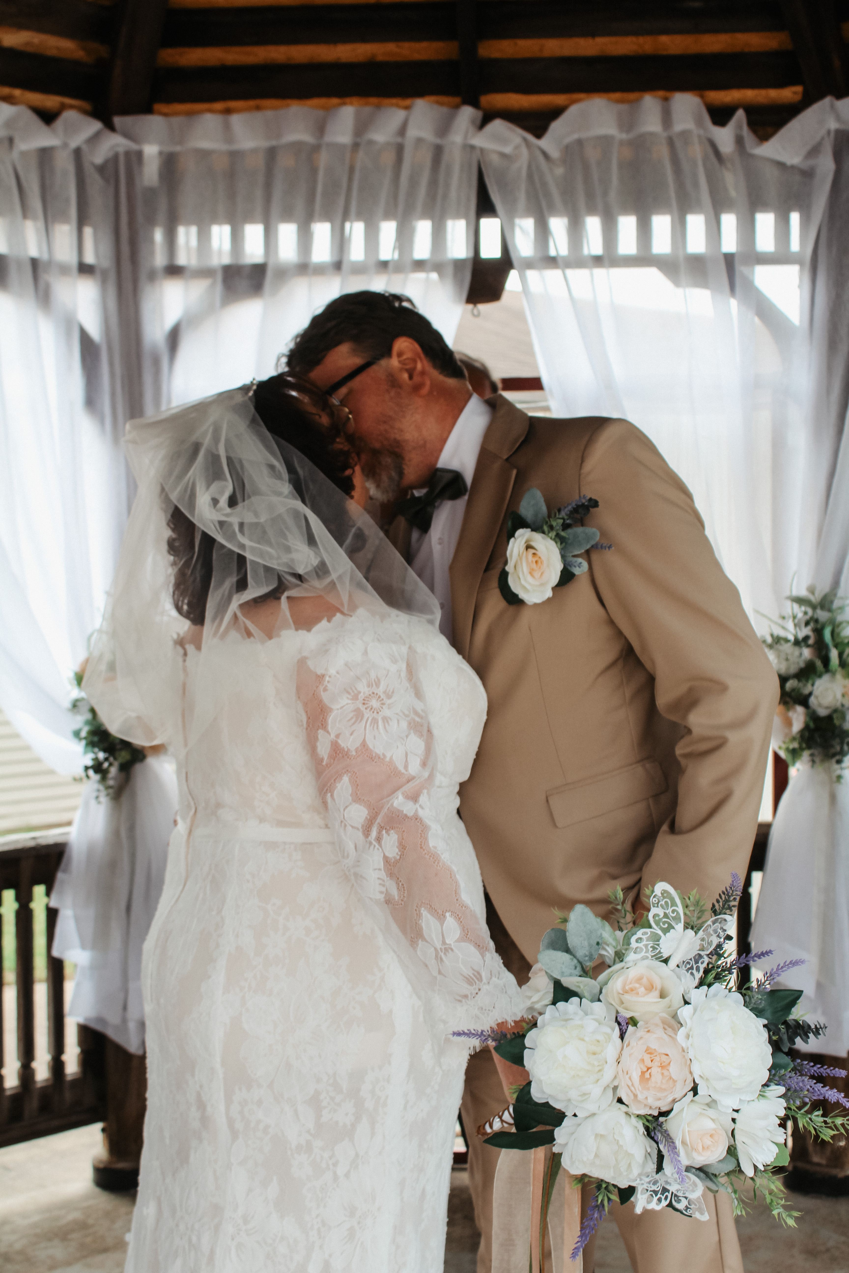 Close-up of bride and groom kiss, bridal bouquet and lace details visible