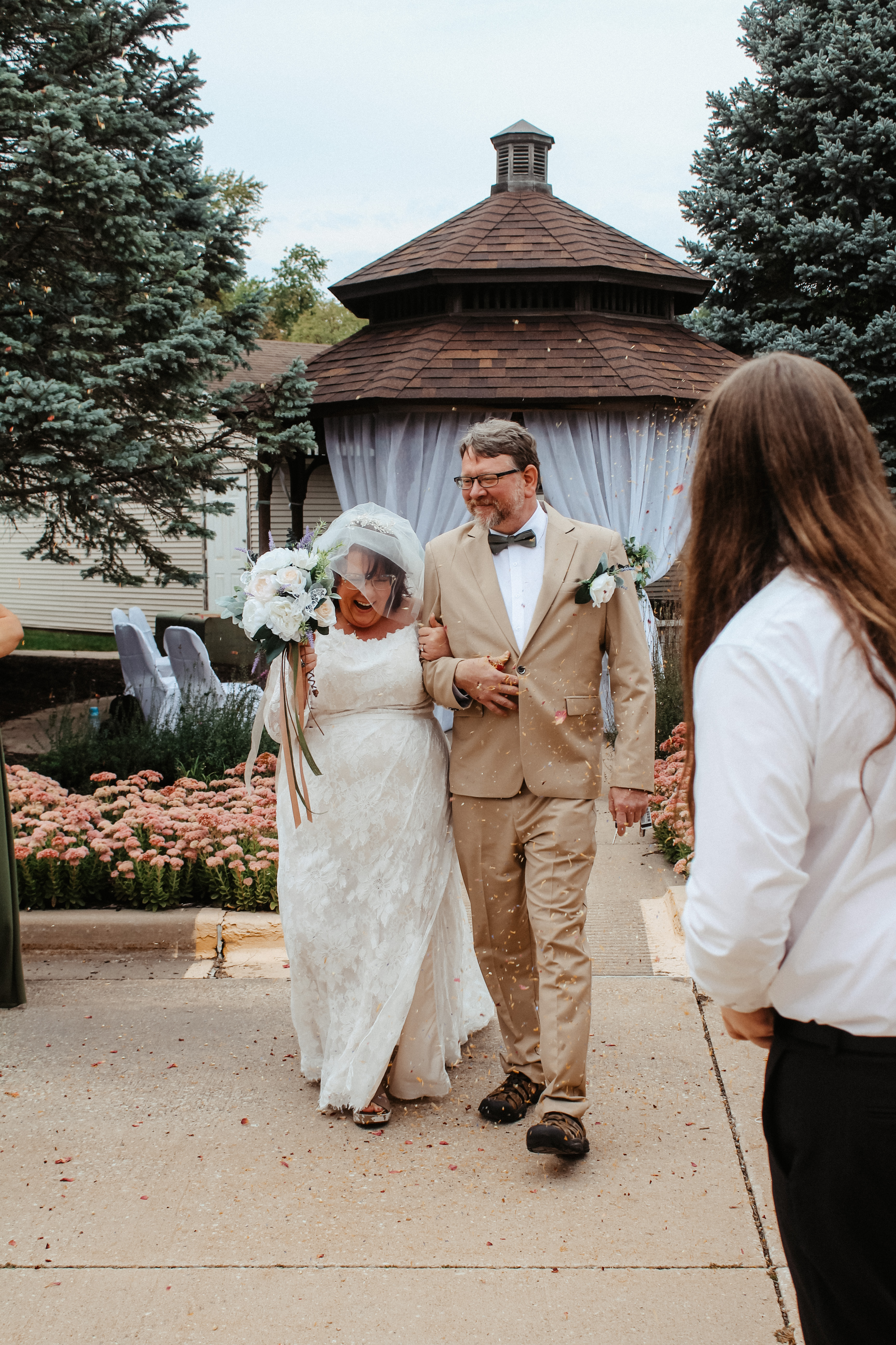 Bride and groom walking outside after ceremony, wedding gazebo with guests in background