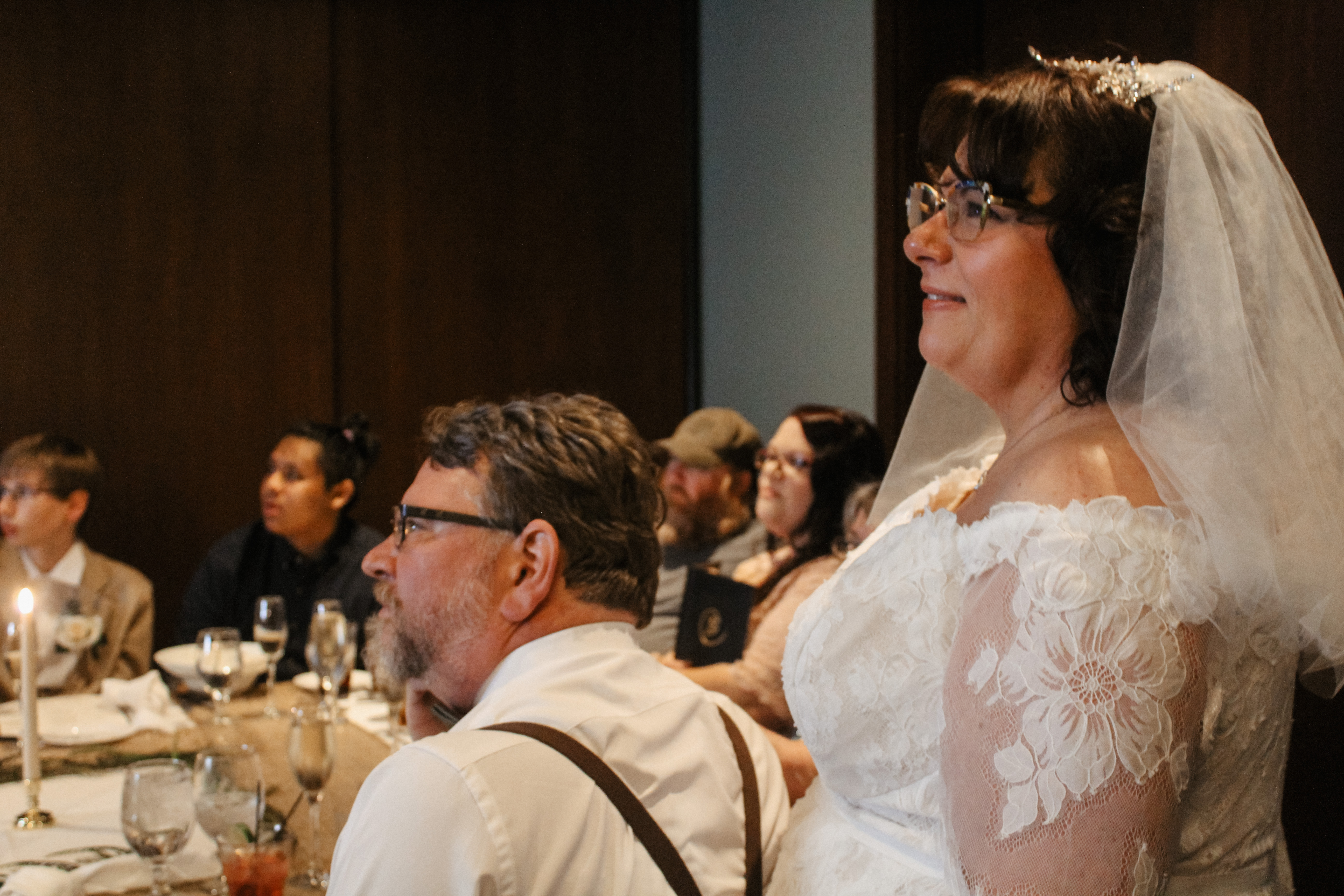 Bride in lace gown smiling with guests, indoor wedding reception candid photo